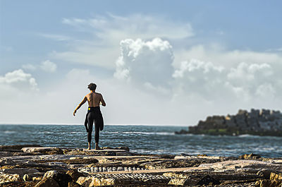 Rear view of man standing on rock by sea against sky