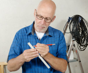 Mature plumber marking on pipe with pencil at workshop