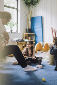 Girl learning guitar from male child care worker at kindergarten