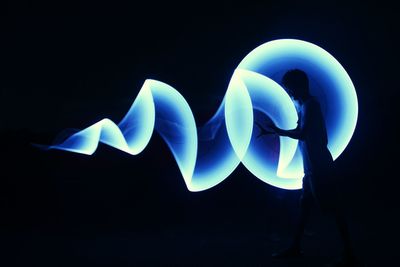 Digital composite image of silhouette man standing with blue light painting against black background