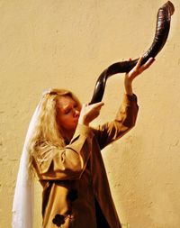 Woman blowing shofar while standing against wall