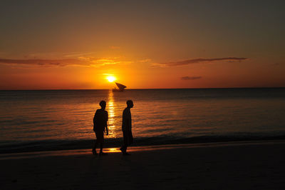 Silhouette men standing on beach against sky during sunset
