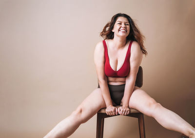 Self loving young woman plus size in underwear sitting on beige background, body love