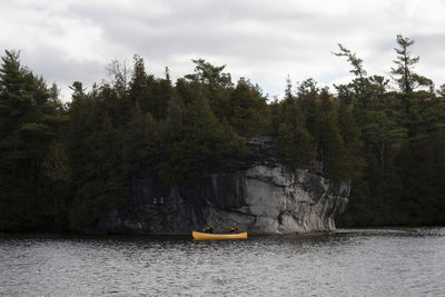 Scenic view of a yellow canoe on a river against cliffs, trees and sky.