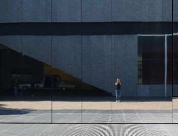 Man reflecting on glass building while standing on sidewalk in city