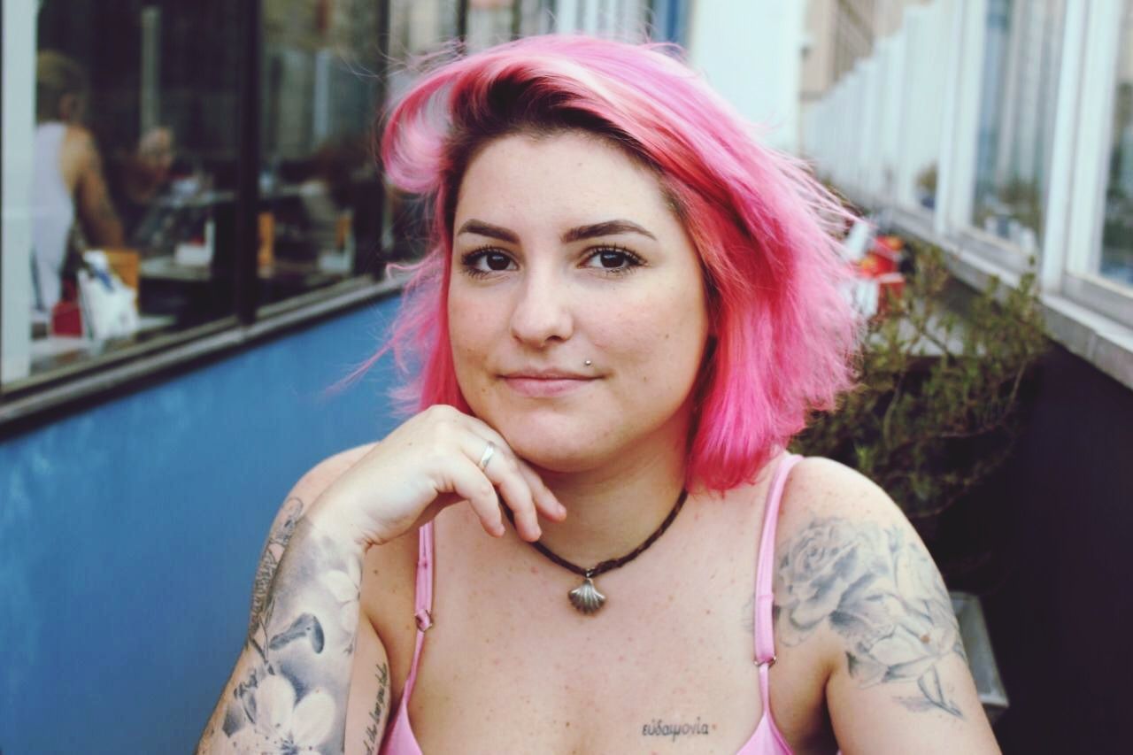 portrait, one person, front view, headshot, lifestyles, real people, looking at camera, young adult, leisure activity, hairstyle, dyed hair, young women, tattoo, women, focus on foreground, pink hair, smiling, casual clothing, pink color, hair, beautiful woman, pierced