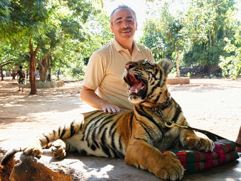 Smiling man sitting with tiger outdoors