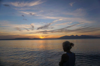 Rear view of woman looking at sea against sunset sky