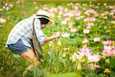 Side view of woman photographing pink lotus water lilies in pond
