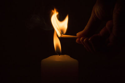 Cropped image of person igniting candle in darkroom