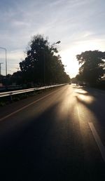 Road by trees against sky during sunset