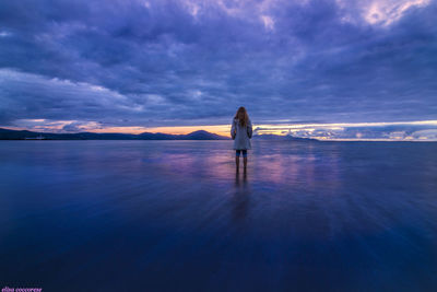 Rear view of man standing by sea against cloudy sky