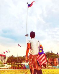 Rear view of man holding flag against sky