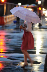 Woman with umbrella walking on illuminated city at night