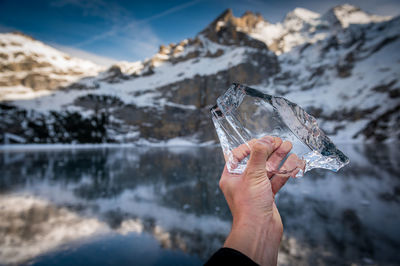 Cropped image of person holding ice by lake against mountains and sky