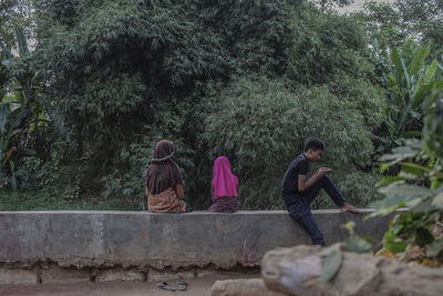 People sitting on retaining wall by plants