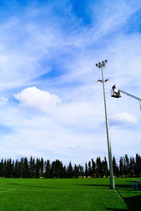 Low angle view of man on cherry picker by floodlight against sky