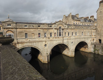 Arch bridge over river against cloudy sky