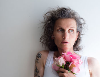 Close-up of woman holding roses while standing against white wall