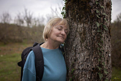 Portrait of young woman standing by tree trunk