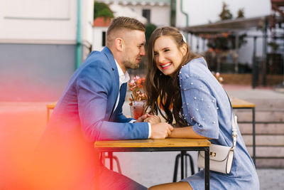 Happy smiling young couple meeting on a date enjoys life sitting at a table, holding hands, in  cafe