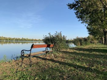 View of park bench on field by lake against sky