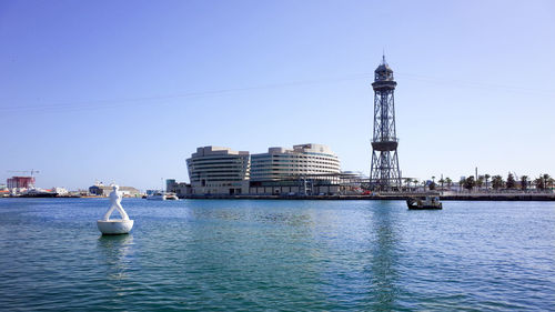 Sailboats in sea by buildings against clear sky