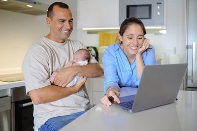 Sensual mother and father with sleeping baby watching photos on laptop