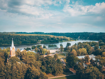 Aerial view of trees and houses by river against cloudy sky