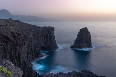 Rocks in sea against sky during sunset