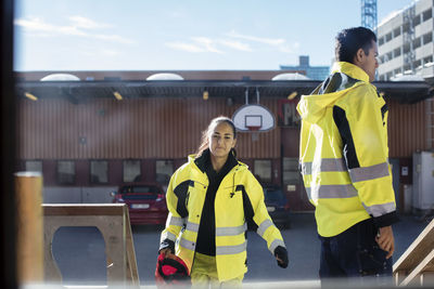 Smiling female auto mechanic student with male friend seen through glass window