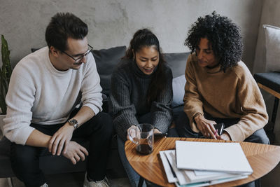 Smiling young businesswoman discussing over digital tablet with male and female colleagues in creative office