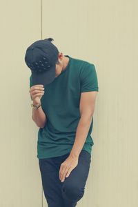 Young man wearing hat standing against wall