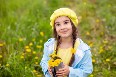 Portrait of a  little girl with two pigtails holds a bouquet of yellow dandelions in a mug, looks up