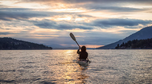 Rear view of silhouette person on shore against sky during sunset