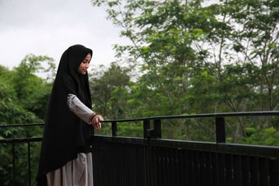 Side view of young woman standing against railing