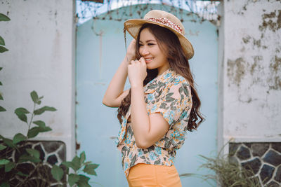 Young woman wearing hat standing against wall