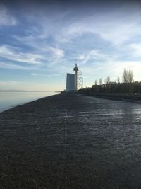 Lighthouse amidst buildings by sea against sky