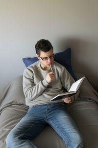 Young man using mobile phone while sitting on bed at home
