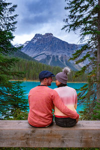 Rear view of couple sitting on mountain against sky