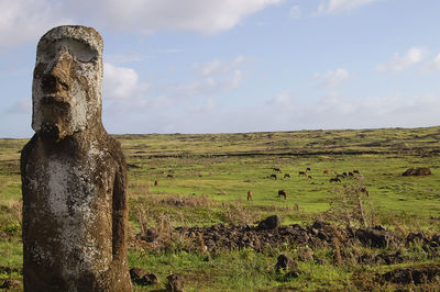 Ancient statue on field against sky