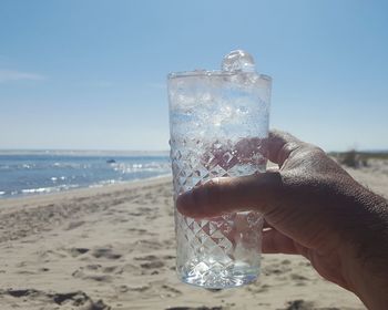 Close-up of hand holding drink at beach against sky