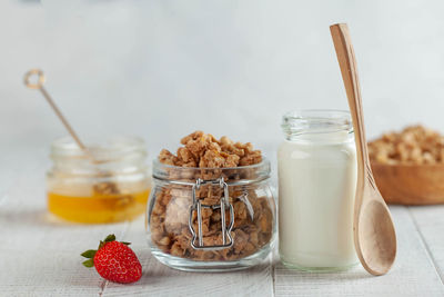 Homemade granola, milk in a jar, honey and strawberries on a wooden background. 