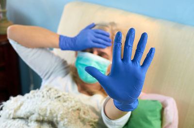 Sick woman lying in a bed with a raised hand showing to keep a distance