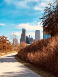 Road by cityscape against sky