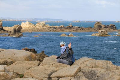 Man sitting on rock by sea against sky