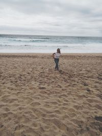 Rear view of woman standing on beach against sky