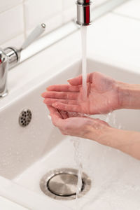 Woman washing hands in fresh water from crane in bathroom. cleanliness, hygiene and health concept