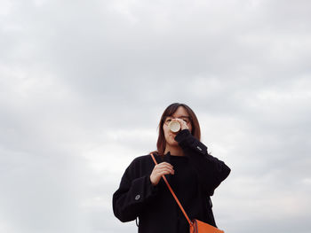 Low angle view of young woman standing against sky