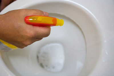 Cropped hand cleaning toilet bowl with spray bottle